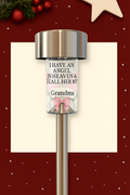 Stainless steel solar memorial light with personalised message for Grandma, featuring angel wings and a pink bow, set against a minimalistic Christmas background with snowflakes and festive greenery.