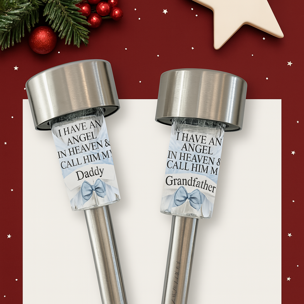 Two stainless steel solar memorial lights with personalised messages for Daddy and Grandfather, featuring angel wings and blue bows, set against a minimalistic Christmas background with snowflakes and festive greenery.