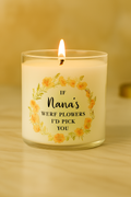 Lit white wax candle in clear glass jar with peach floral wreath and “If Nana’s Were Flowers I’d Pick You” black text, styled on marble with beige background.