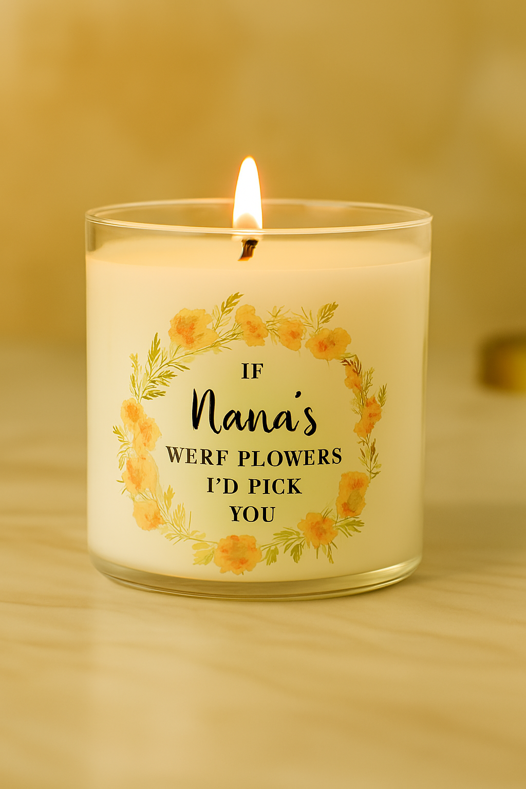Lit white wax candle in clear glass jar with peach floral wreath and “If Nana’s Were Flowers I’d Pick You” black text, styled on marble with beige background.