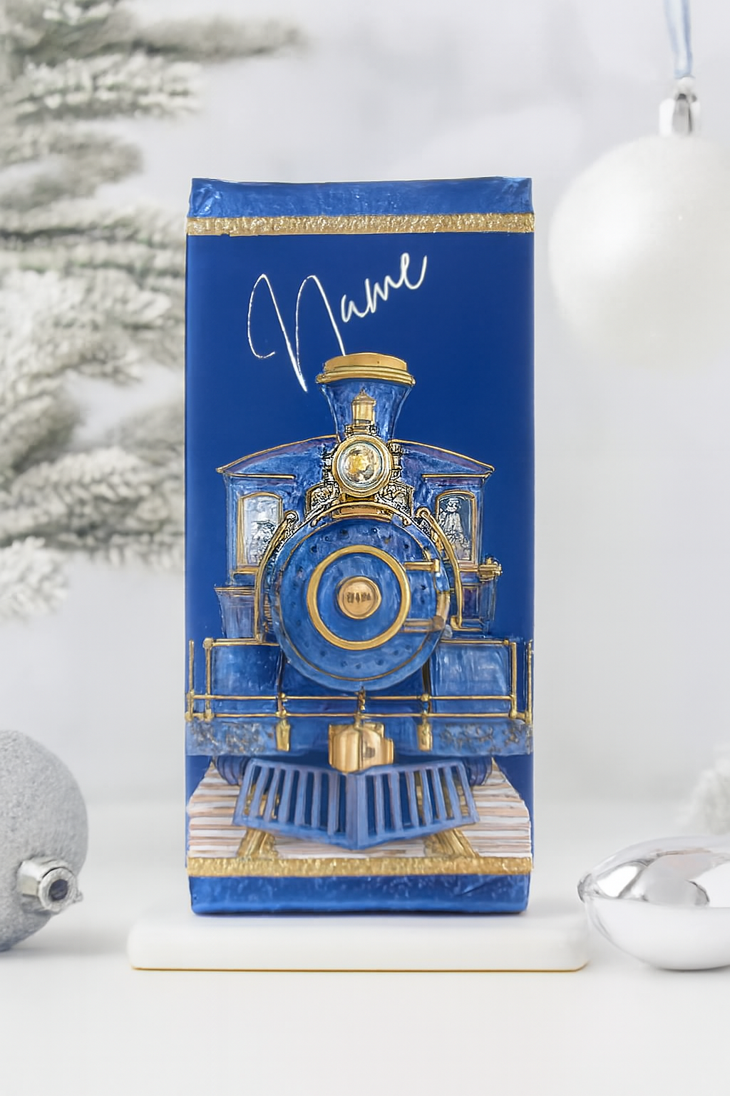 Personalised royal blue and gold Christmas train chocolate bar standing upright against a snowy white and silver festive background. Features a vintage steam locomotive illustration with ornate gold accents and a customisable name in white script. Available with Galaxy, Dairy Milk, or as a wrapper-only option.