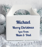 White personalised Christmas gift box with blue text reading “Michael Merry Christmas Love From Mum & Dad,” styled on a snowy silver background with glittery baubles, frosted pine branches, and silver bead garland for a festive, elegant presentation.