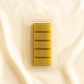Luxury golden wax melt clamshell with five glitter-infused bars, packaged in clear plastic and displayed on soft cream satin fabric
