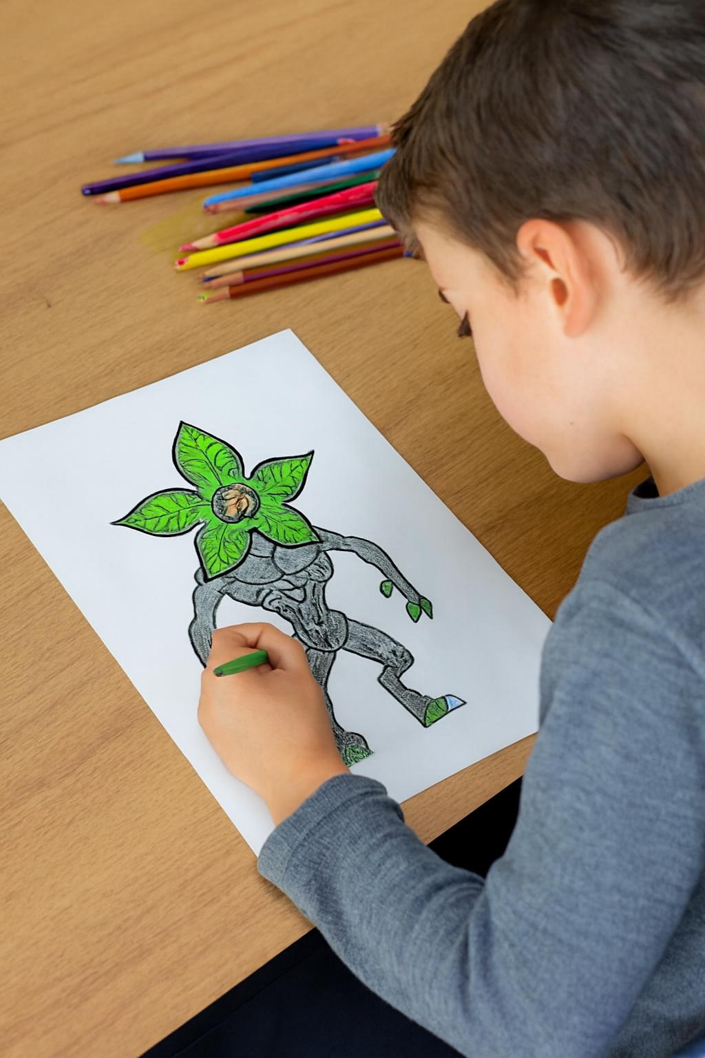 Child coloring a picture of a creature with plant-like features on a piece of paper.