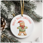 White ceramic ornament featuring a cheerful gingerbread figure in a green sweater and red scarf, with “HOLLY JOLLY CHRISTMAS” in red text, hanging from a gold ribbon on a snowy pine branch.