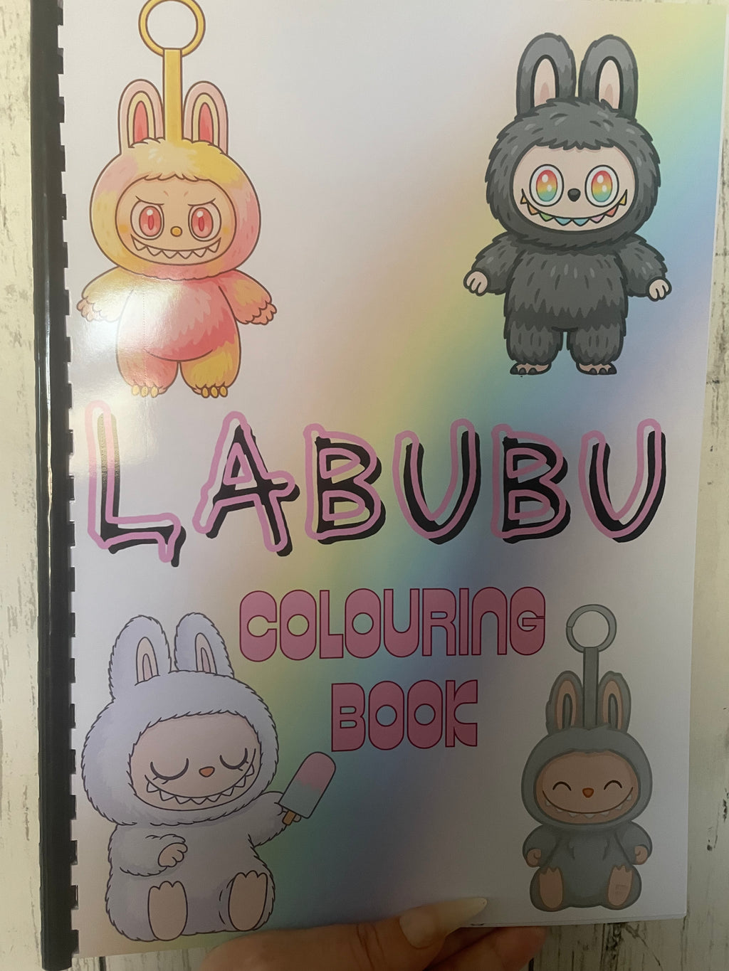 Labubu Colouring Book with pastel rainbow background and four cute bunny-monster characters on the front cover, featuring comb binding and colourful illustrated designs