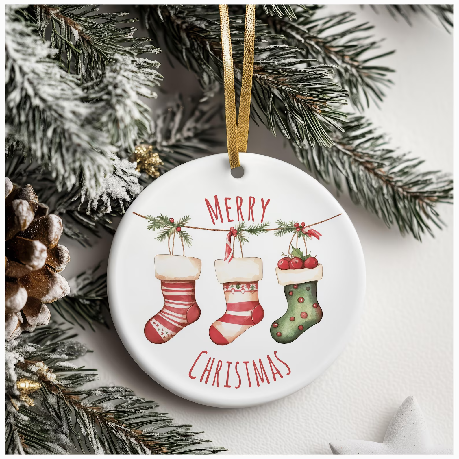 Ceramic ornament showing three festive stockings hanging from a pine branch, with candy canes and berries, surrounded by pine needles and a white star, with “MERRY CHRISTMAS” in red.